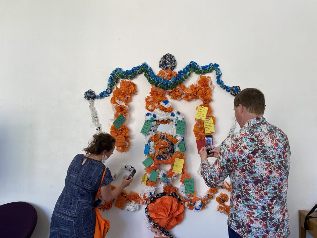 Two people arranging coloured paper decorations on a wall in the form of an altar.