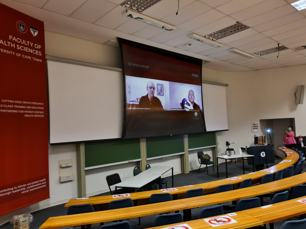 Photo of a classroom with Zoom call showing on a projection screen.