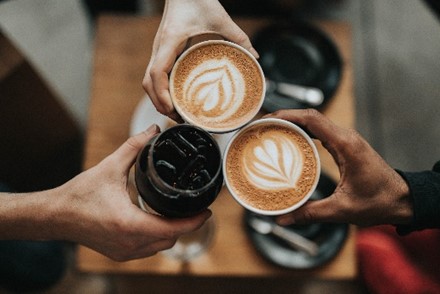 Photo of three hands holding coffees and a soft drink together