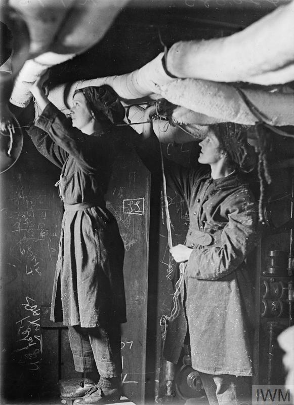 Women workers sewing canvas covers on pipes between the decks of a ship in a shipbuilding yard (IWM, Q 20085)