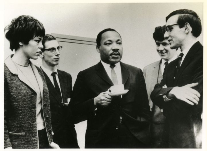 Photograph depicts civil rights activist Dr Martin Luther King speaking with Newcastle University students over an informal coffee morning during his visit to Newcastle University to accept an honorary doctorate of Civil Law on 13th November 1967. Among the students shown are Meredyth Bell (nee Patton), Deputy President of the Students Representative Council (far left), and C. B. 'Nick' Nicholson, President of the Students' Representative Council (far right). 