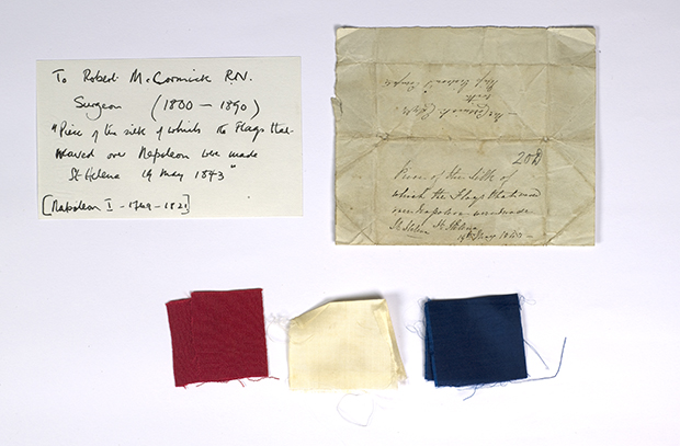 contains pieces of red, white and blue silk. An accompanying scrap of paper reads "Pieces of the silk of which the flags that waved over Napoleon were made. St-Helena 19 May 1843"