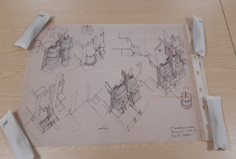 An A2 sized piece of transparent paper laid flat on a wood effect table with rectangular map weights at each corner.  The designs on the paper contain rear elevation sketches of a 4 storey house. The image is to demonstrate an example of drawings found within an architectural collection. 