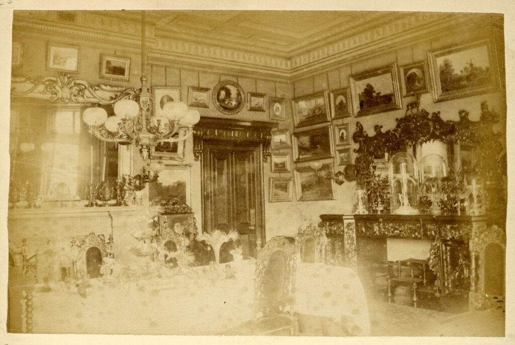 Sepia photograph of inside of the house, showing floor-to-ceiling walls of paintings and fine furniture.