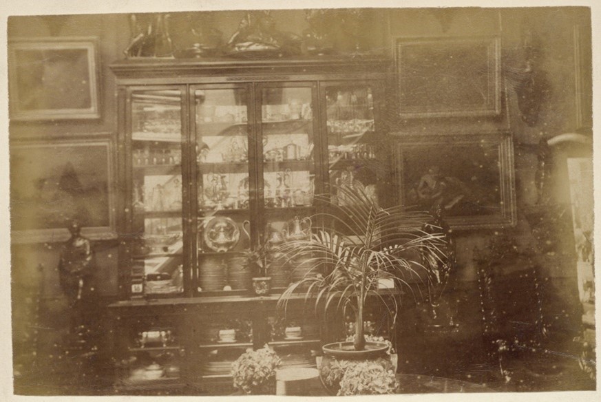 Sepia photograph of inside the house, showing a large glass cabinet with glassware inside.