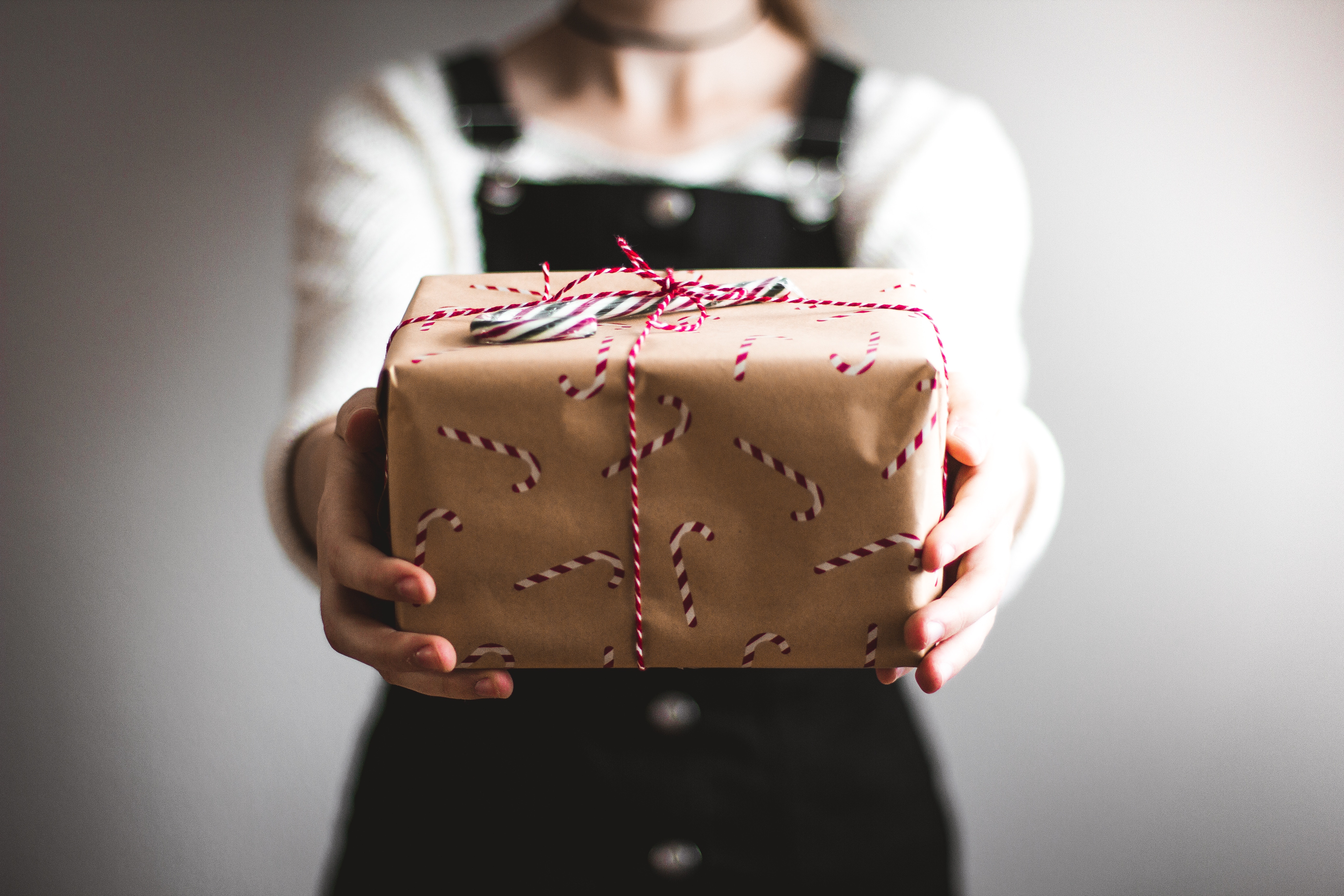 Person holding a gift box wrapped in brown paper with candy stripe ribbon.