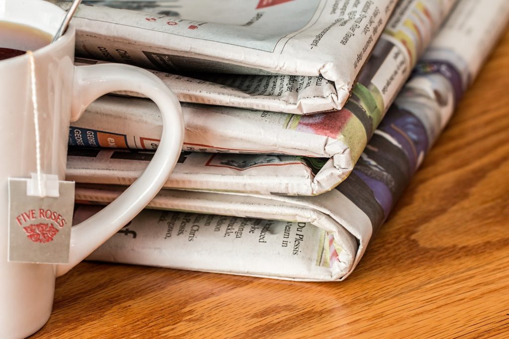 Three newspapers piled on a desk next to a mug of tea.